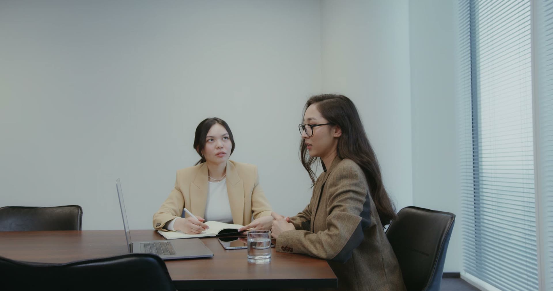Two colleagues talking over papers at a meeting table in a bright office.