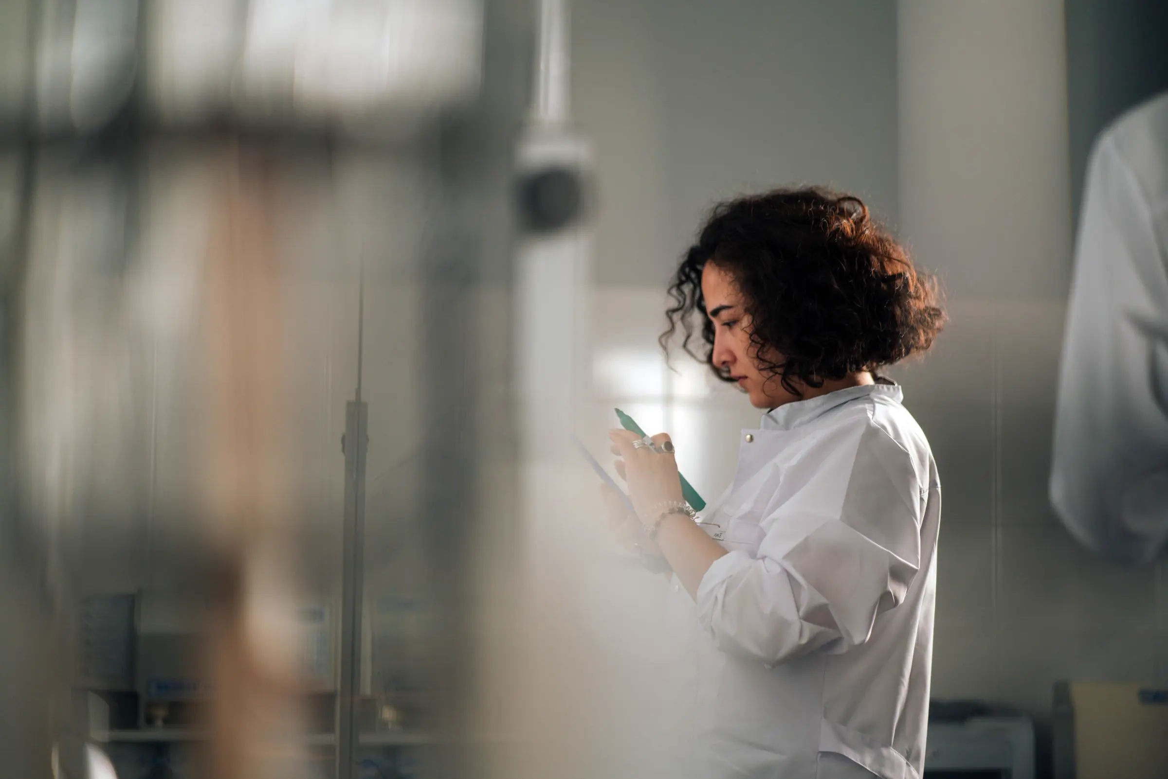 A scientist in a white lab coat checking her phone between tasks in the lab.