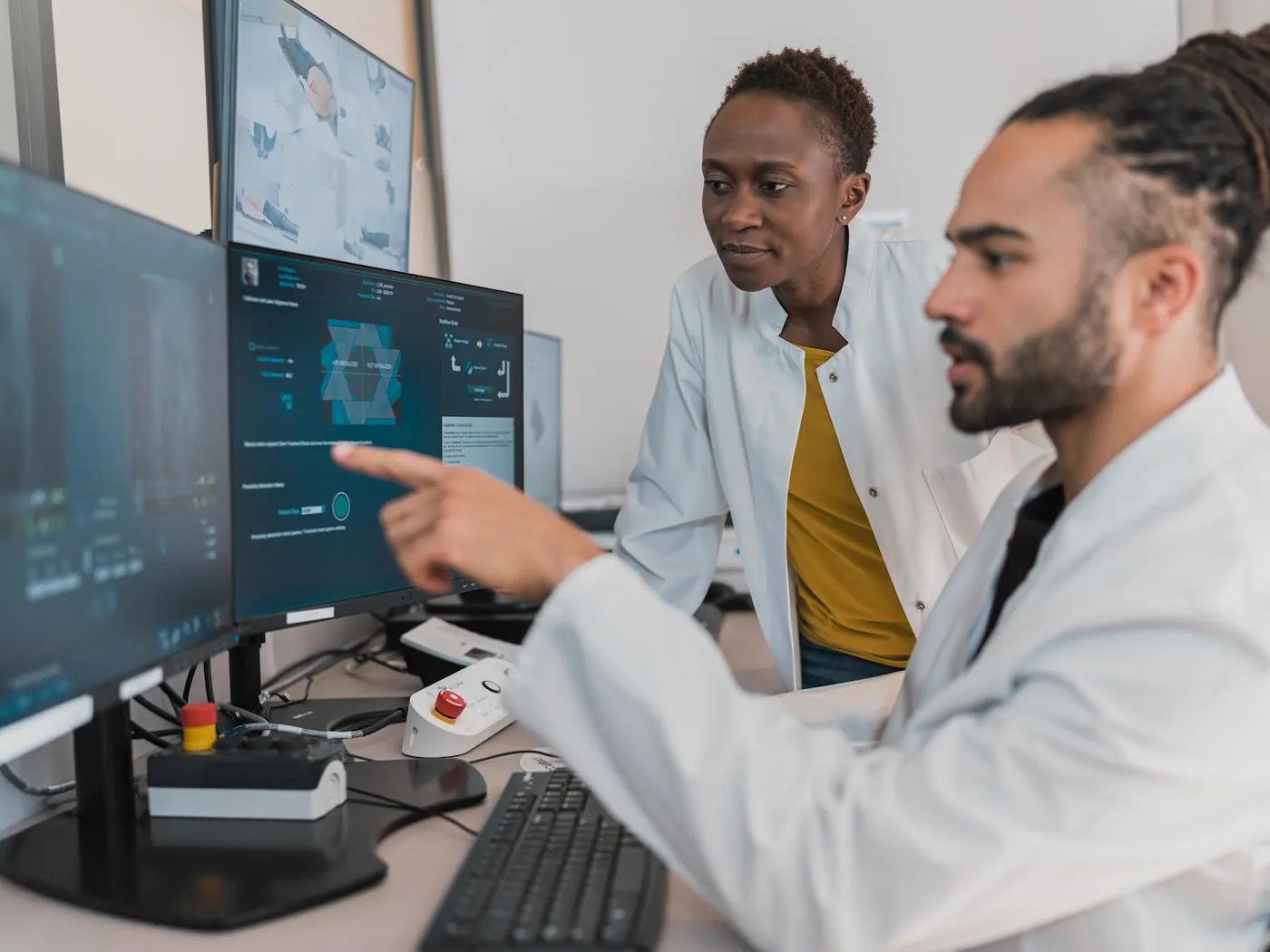 Two scientists in white coats discussing data on a pair of monitors, one pointing at the screen.
